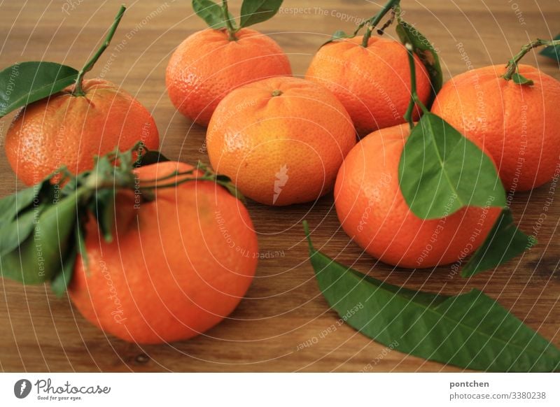 Sieben Mandarinen mit grünen Blättern liegen auf einem Holztisch Lebensmittel Frucht Ernährung Bioprodukte Diät sauer orange Blatt Tisch Gesundheit