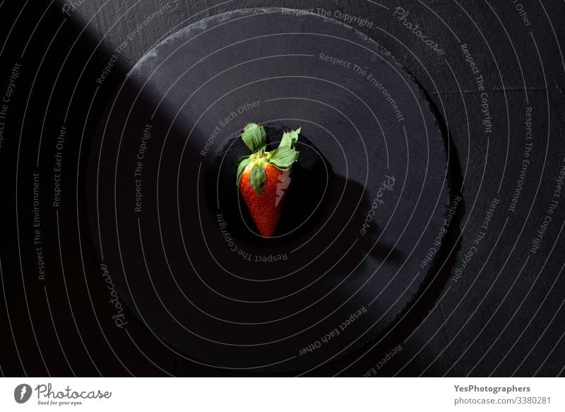 Einzelne Erdbeere auf schwarzer Platte in grellem Licht. Frucht Dessert Bioprodukte Gesunde Ernährung frisch obere Ansicht ganz schwarz schwarzer Hintergrund