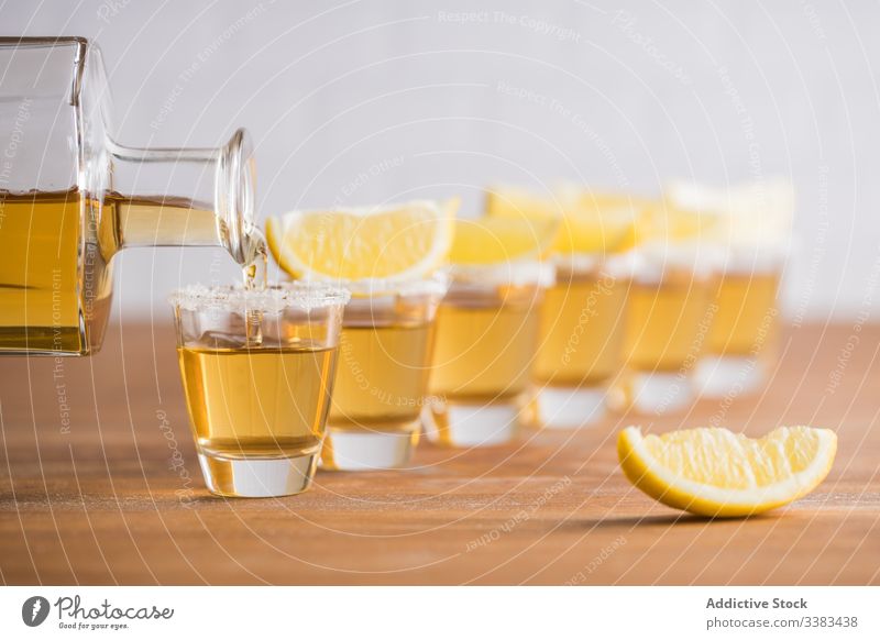 Schuss Alkohol mit Zitronenscheiben oben drauf Tequila Scheibe Spielfigur Schnaps Reihe Glas Tisch hölzern Wand trinken Getränk Erfrischung geschmackvoll kalt
