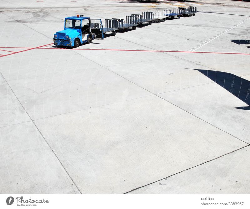 Gepäckwagen ohne Gepäck auf dem Flughafen an der Parkposition eines schattenwerfenden Flugzeuges Transport Zugmaschine Anhänger Markierungen Linien rot blau