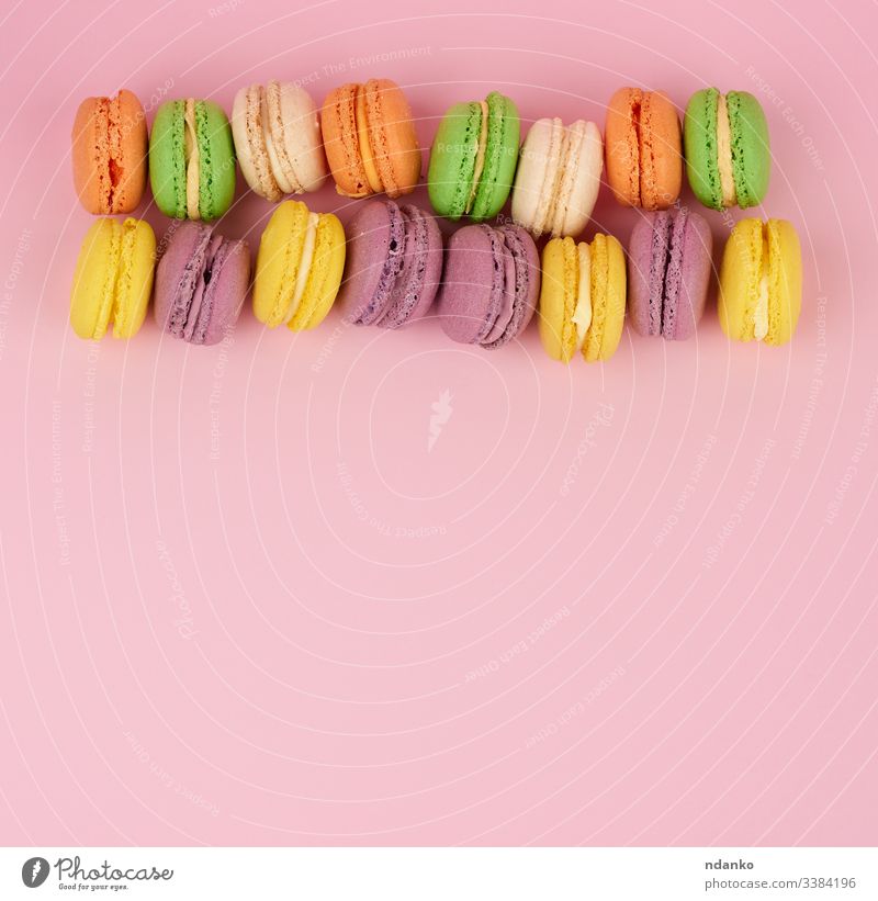 gelbe, violette runde gebackene Makkaronentorten auf rosa Hintergrund, Dessert liegt in einer Reihe Macaron Makrone Schaumgebäck niemand Gebäck Haufen purpur