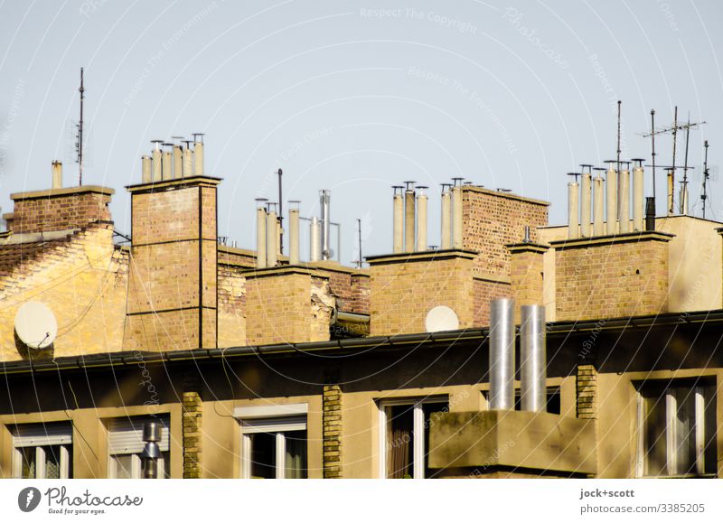 Sammlung von Schornsteinen und paar Antennen nebeneinander Dach Symmetrie Nostalgie Wolkenloser Himmel Fenster oben Sonnenlicht Hintergrund neutral Mietshaus