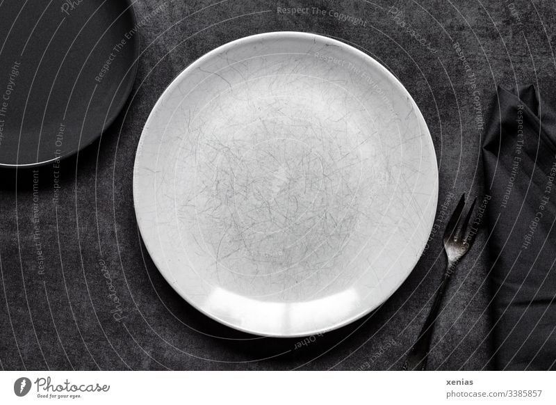 Heller und dunkler runder Teller mit Gabel auf grauem Untergrund leer Foodfotografie weiß Innenaufnahme Ernährung Serviette Tisch schwarz zerkratzt Essen dunkel