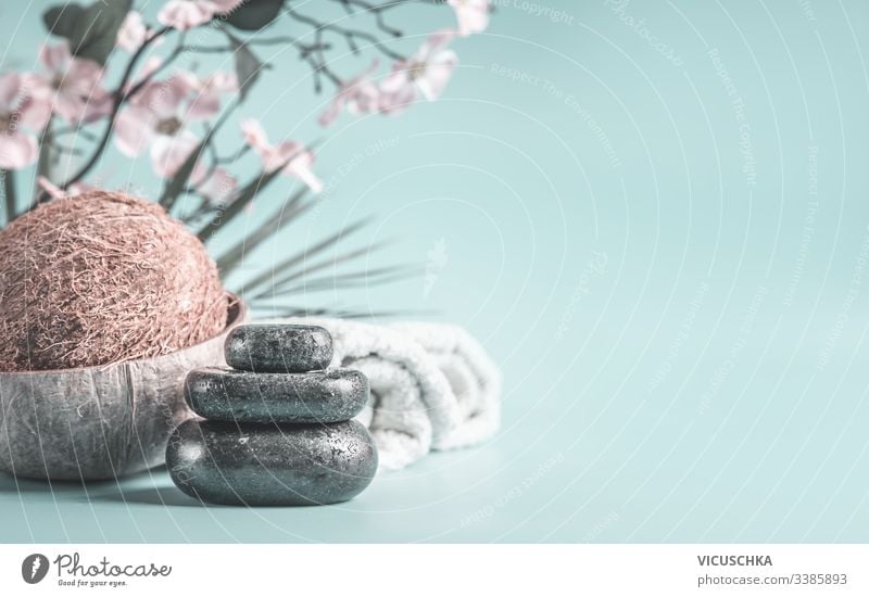 Zen-Steine mit Kokosnuss und Handtüchern auf hellblauem Hintergrund mit Blumen. Entspannender Schönheitstag. Spa-Konzept Licht Tag niemand Erholung Nahaufnahme