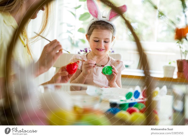 Eine Mutter und eine Tochter feiern Ostern und bemalen Eier mit dem Pinsel. Eine glückliche Familie, die lächelt und lacht. Ein süßes kleines Mädchen in Hasenohren, das den Feiertag vorbereitet.