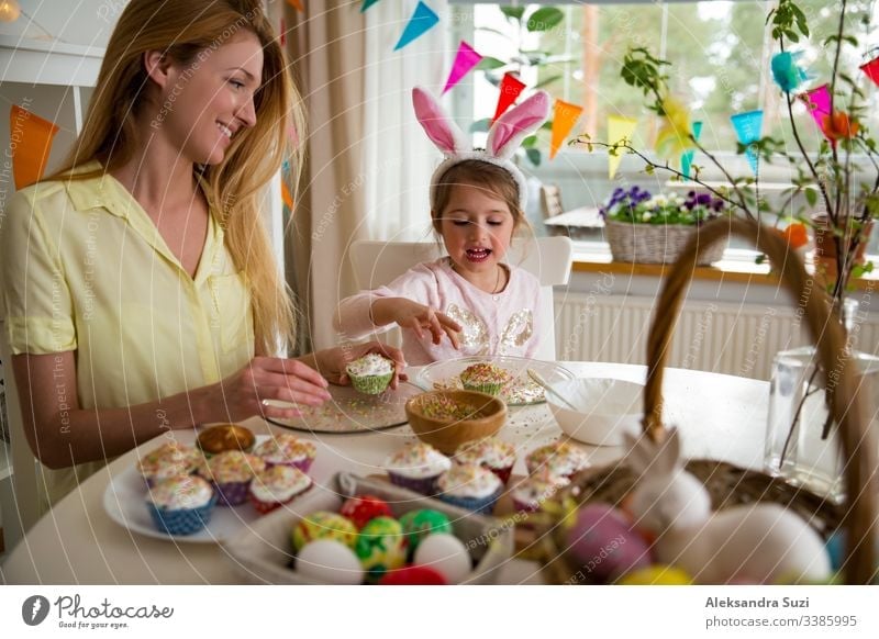 Mutter und Tochter feiern Ostern, kochen Muffins, mit Glasur überzogen. Fröhlicher Familienurlaub. Süßes kleines Mädchen in Hasenohren. backen offen Feier Kind
