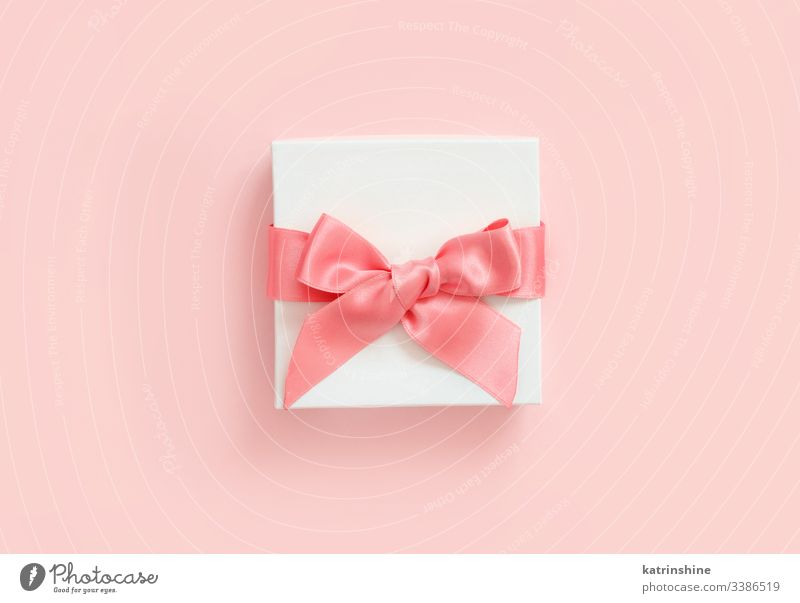 Weiße Geschenkverpackung mit Schleife auf hellrosa Hintergrund weiß Bändchen Liebe romantisch Draufsicht oben präsentieren Konzept kreativ Tag Dekor