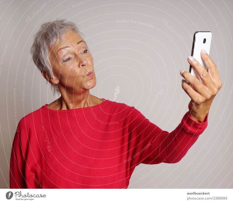 ältere Frau macht Duckface für Selfie mit Smartphone Selbstportrait Kussmund Senior Fotokamera Telefon Dame Erwachsener lustig Ausdruck 60 trendy selbstbewusst
