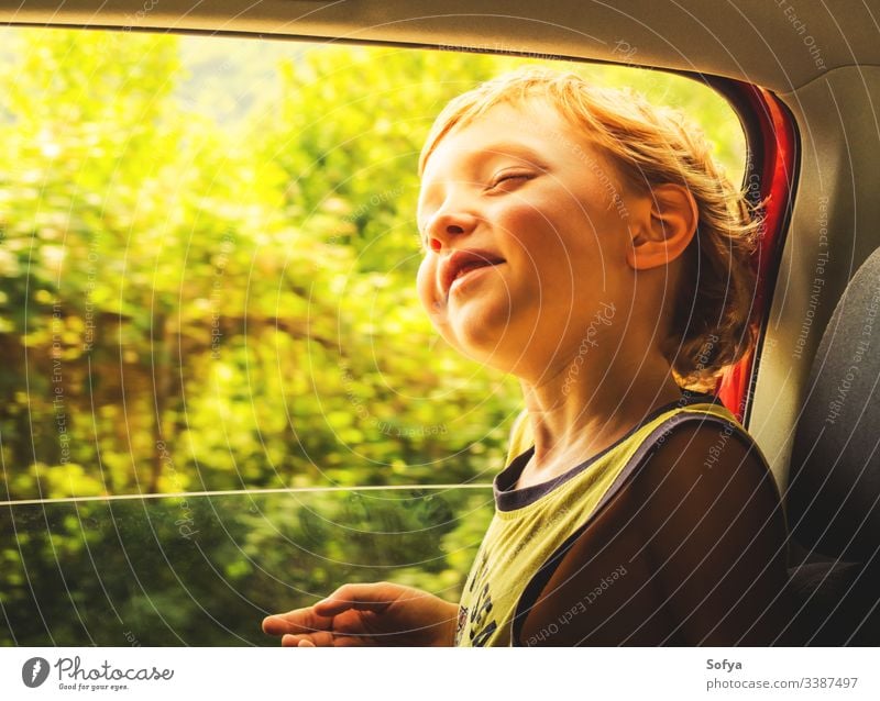 Kleiner kaukasischer Junge, der Sonne und Wind genießt und in einem Auto mit offenem Fenster fährt. wenig Kind PKW reisen Glück Haut Emotion Moment Behaarung