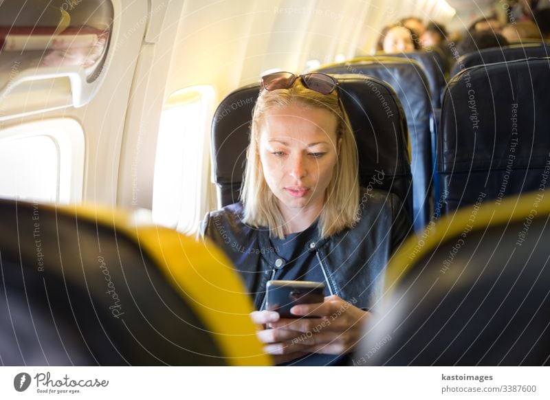 Frau, die während eines kommerziellen Fluges im Flugzeug das Mobiltelefon als Unterhaltungsgerät benutzt. Aussehen Ebene Blick Air Fluggerät Verkehr Transport