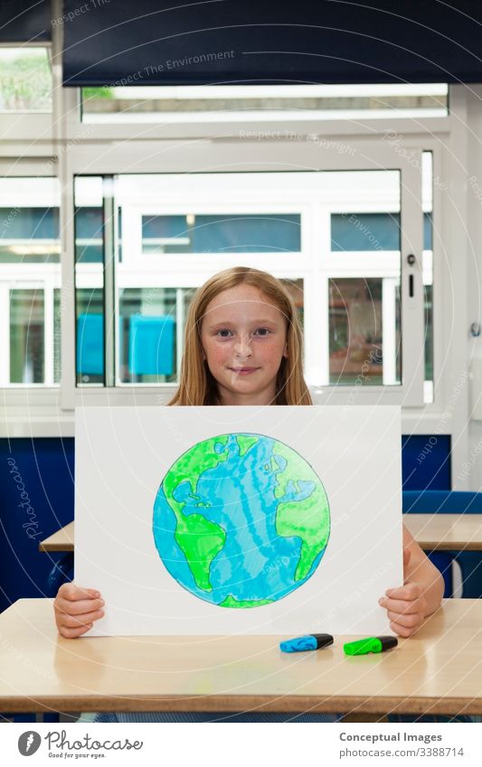 Kaukasisches Mädchen in der Grundschule hält ein Plakat mit einem Bild der Erde Zeichnung Planet Schulkind Umwelt Frau Kind Bildung Ökologie Zukunft Erhaltung