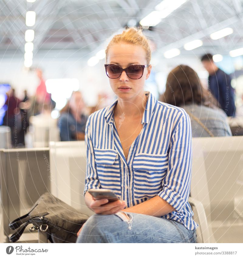 Frau benutzt ihr Handy, während sie an den Abfluggates des internationalen Flughafens auf das Einsteigen in ein Flugzeug wartet. reisen Sitzen Fahrkarte Telefon