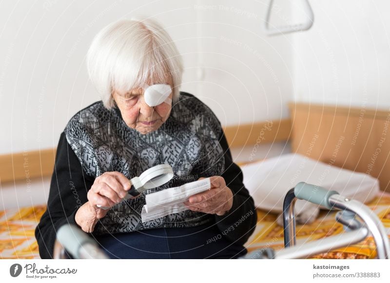 Sehbehinderte ältere Frau, 95 Jahre alt, sitzt am Bad und versucht mit der Lupe zu lesen. Senior Sehvermögen Augenlicht sehbehindert Rentnerin Pflege