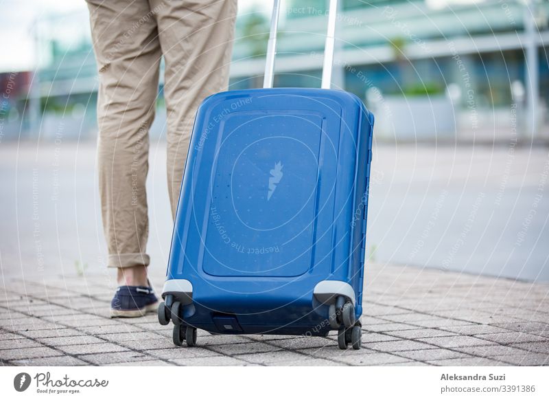 Stilvoller Mann, der mit einem blauen Koffer zum Flughafen geht. Geschäftsmann auf Reisen. Ankunft Tasche Gepäck Gebäude Business führen Fall lässig Großstadt