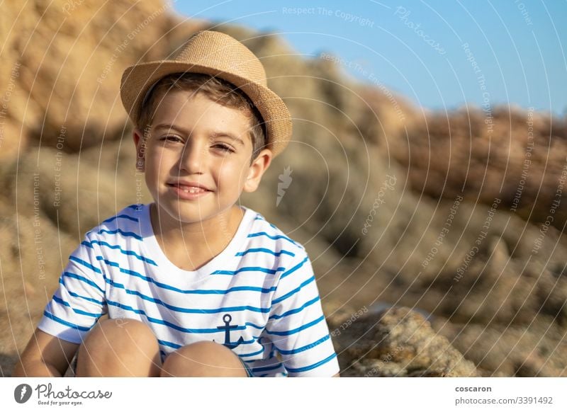 Porträt eines niedlichen Kindes, das auf einem Felsen in der Nähe des Meeres sitzt Anker Baby Hintergrund Strand schön blond blau Junge hell Kaukasier Kindheit