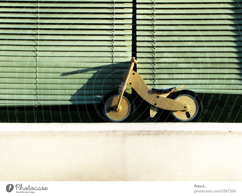 Das kleine Laufrad wartet vor verstaubten Schaufensterrollos sehnsücht darauf, endlich gekauft zu werden Außenaufnahme Spielen Fahrrad warten Rollos allein Holz