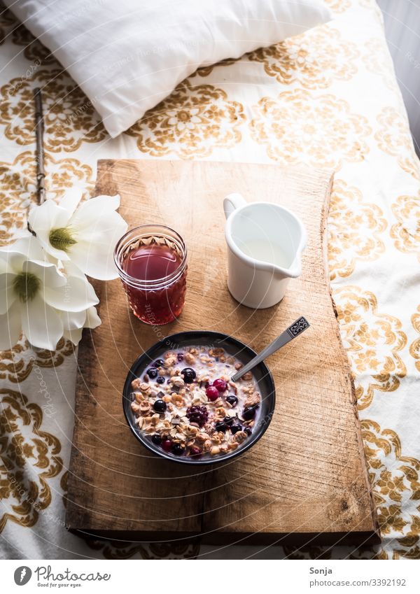 Romantisches Frühstück mit Müsli, Milch und frischen Beeren auf einem Holzserviertablett im Bett muesli milch himbeere heidelbeere bett retro holzbrett löffel