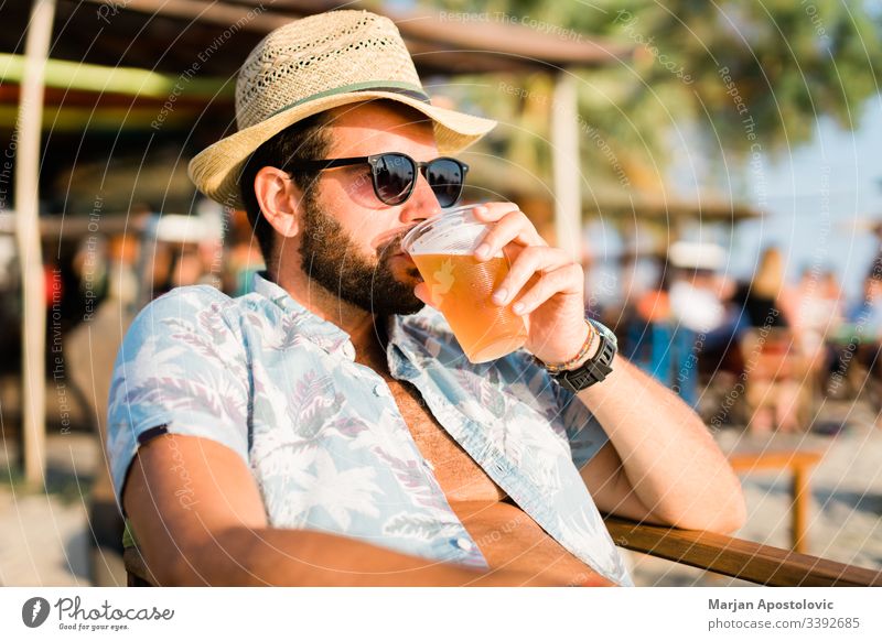 Junger Mann trinkt Bier in einer Strandbar und genießt den Sonnenuntergang 30s Erwachsener Alkohol allein Bar bärtig Getränk lässig Kaukasier jubelt cool