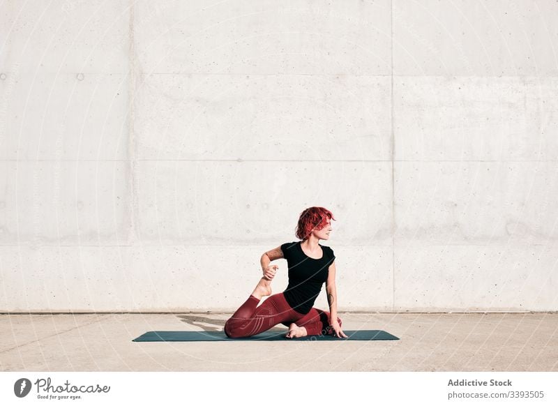 Flexible barfüßige Frau, die beim Training auf der Straße ihren Körper in gefesselter Schwanenhaltung dehnt Dehnung Yoga beweglich gebundene Schwanenhaltung