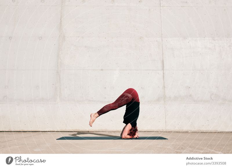 Frau macht Gleichgewichtsübung im Kopfstand, während sie Yoga auf der Straße praktiziert Übung akrobatisch üben Training urban sirsasana Beton stark beweglich