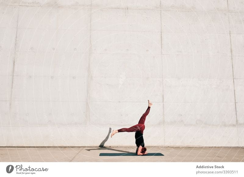 Frau macht Gleichgewichtsübung im Kopfstand mit geteilter Pose während sie Yoga auf der Straße praktiziert Übung akrobatisch üben Training urban sirsasana Beton