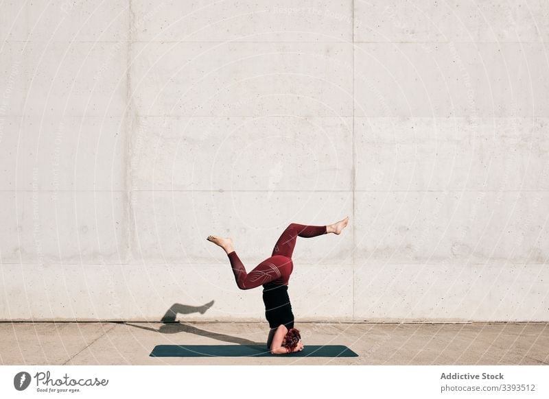 Frau macht Gleichgewichtsübung im Kopfstand mit geteilter Pose während sie Yoga auf der Straße praktiziert Übung akrobatisch üben Training urban sirsasana Beton