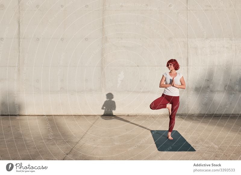 Frau macht Gleichgewichtsübung in Baumhaltung während sie Yoga auf der Straße praktiziert Athlet Namaste meditieren üben Training Übung Dehnung Barfuß Beton