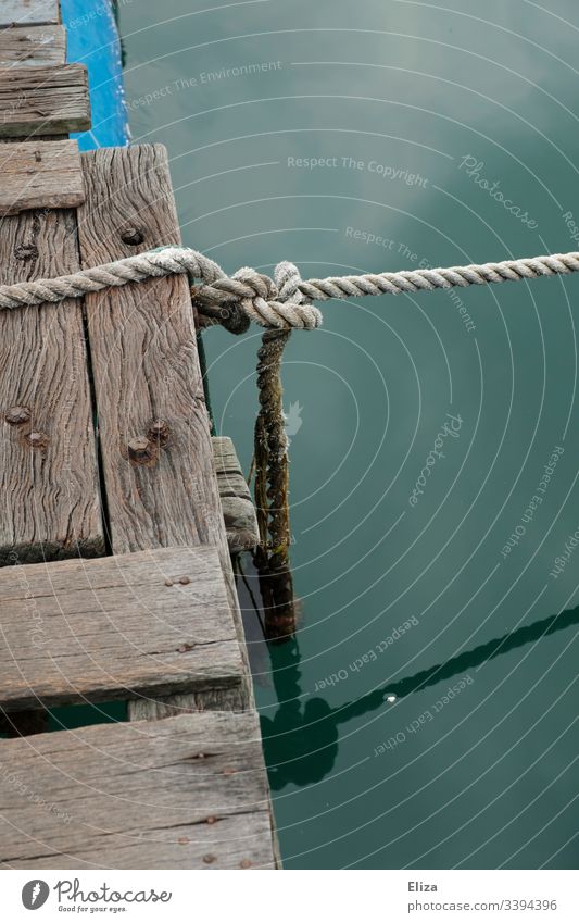 Ein Holzsteg mit einem Tau und einem Knoten über türkisem Wasser Holzssteg Steg verknotet Meer maritim fest vertaut festbinden festgebunden Seil Menschenleer