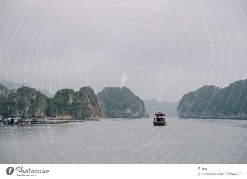 Ein Ausflugsschiff in der Halong Bay in Vietnam; schöne Landschaft mit Kalksteinfelsen, die aus dem Meer ragen, bei nebligem Wetter Schiff Boot Sehenswürdigkeit