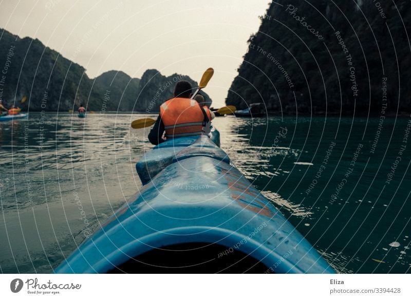 Kajafahrende Touristen in blauen Kajaks mit Orangen Schwimmwesten in der Halong Bay in Vietnam Meer Kajakfahren Wasser Aussicht Sport Abenteuer Felsen Natur