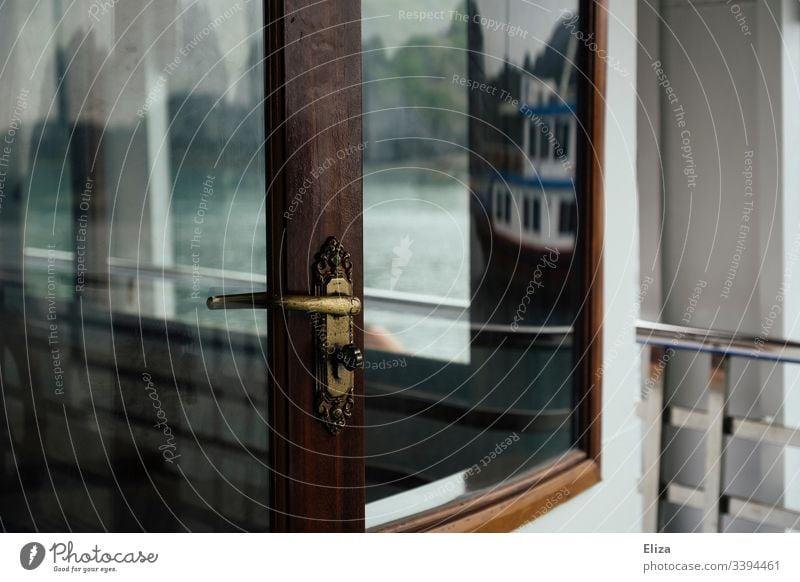 Detailaufnahme einer goldenen Türklinke an einer Glastüre vor einem Fenster mit Holzrahmen auf einem Schiff türklinke Spiegelung Boot Türschloss Reling Ausflug