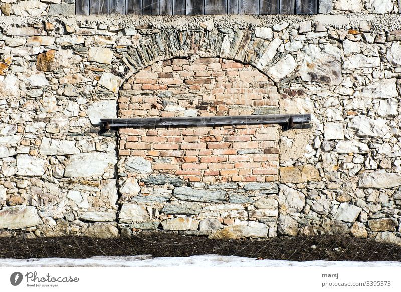 Eine Steinmauer mit einem zugemauerten Tor, das zusätzlich mit einem Balken gesichert ist. Fachmännisch gemauerter Torbogen. lockdown Mauer Türsicherung