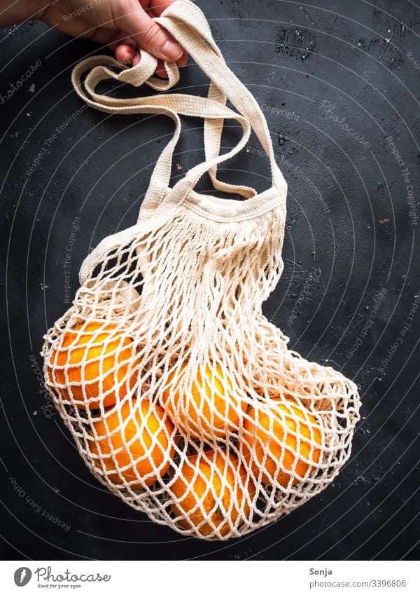 Hand mit einer wiederverwendbaren Einkaufstasche und frischen Orangen auf einem schwarzen Hintergrund orange einkaufstasche halten Gesunde Ernährung Frucht