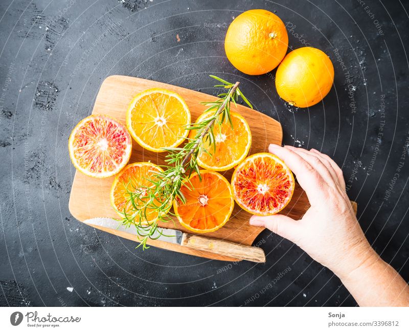 Hand mit frischen halbierten Orangen auf einem Holzschneidebrett auf einem schwarzen Hintergrund Frau orange holz messer rustikal draufsicht Frucht Arme