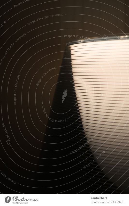 Moderner Lampenschirm mit Linien in Nahaufnahme vor dunkler Wand, abstrakt mit Schattenwurf Licht dunkel menschenleer Textfreiraum links Textfreiraum oben