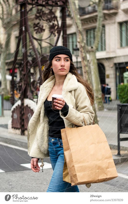 Porträt einer jungen europäischen Frau, die in einer Straße der Stadt spazieren geht, mit Kaffee zum Mitnehmen in der Hand modern allein schön Tasse attraktiv