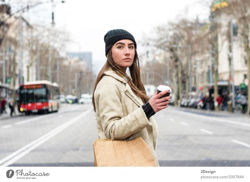 Porträt einer jungen europäischen Frau, die in einer Straße der Stadt spazieren geht, mit Kaffee zum Mitnehmen in der Hand modern allein schön Tasse attraktiv