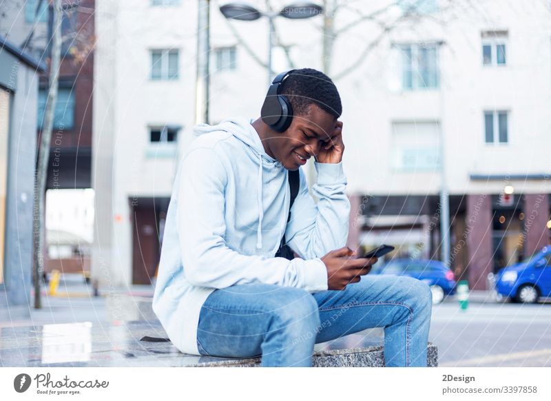 Junger schwarzer Mann sitzt auf einer Bank und hört Musik über Kopfhörer Technik & Technologie Lifestyle männlich Freizeitkleidung trendy Glück Afrikanisch