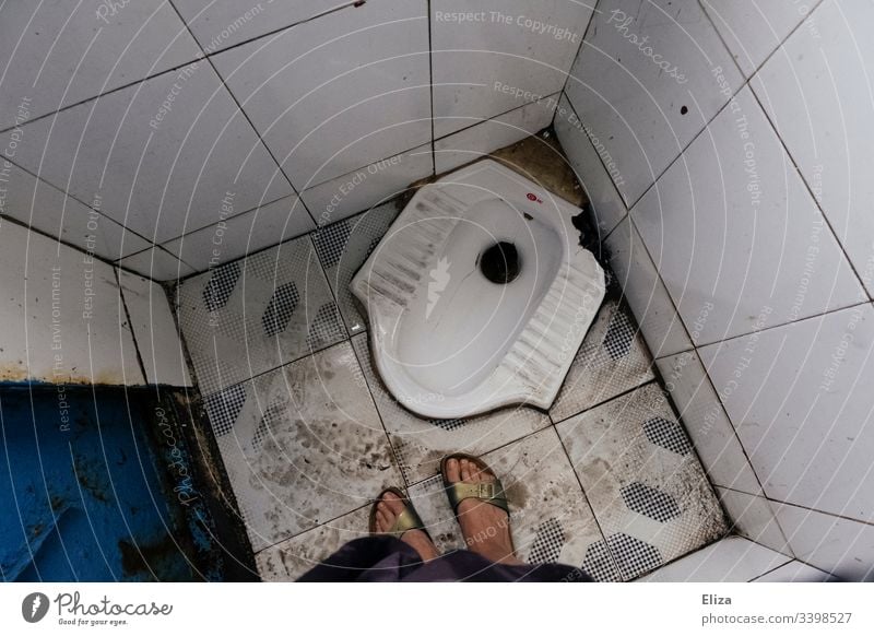 Eine Vogelansicht einer dreckigen Toilette zum Hocken mit weiblichen Füßen drauf in Südostasien Asien hocken ungewohnt Klo Frau eklig Reisen Farbfoto