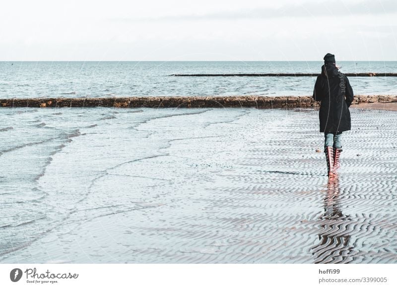 Frau mit rot gestreiften Gummistiefeln geht im Winter allein am Strand spazieren rote Gummistiefel Beine Stiefel Nordseeküste Wattenmeer Landschaft Umwelt