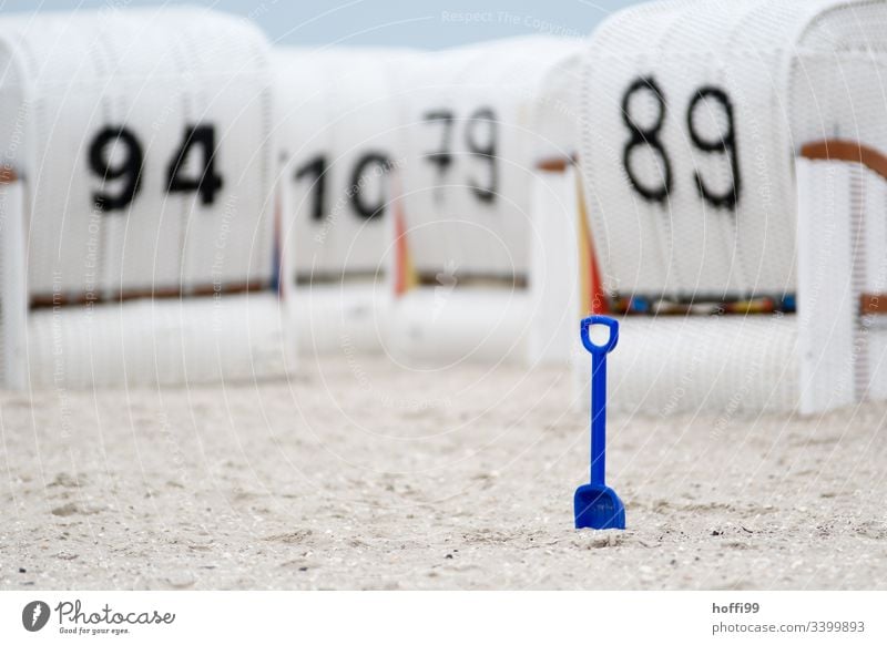 blaue Schaufel im Fokus vor unscharfen weißen Strandkörben am Strand Strandkorb Kinderschaufel Urlaub Erholung Küste Meer Sand Ostseestrand