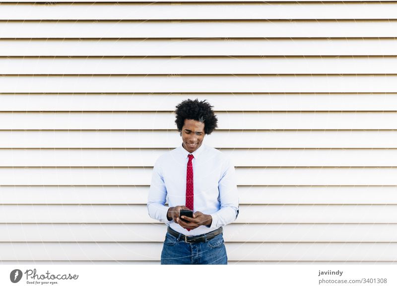 Schwarzer Geschäftsmann mit einem Smartphone mit weißem Jalousien-Hintergrund schwarz lockig Afro-Look Business du Behaarung Anzug Afrikanisch männlich