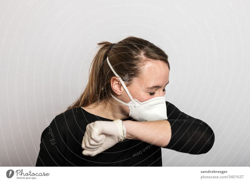 Frau mit Mundschutz und Einmalhandschuhen niest in die Armbeuge Coronavirus COVID-19 Virus Krankheit Pandemie Epidemie Maske Schützen Handschutz Steril Medizin