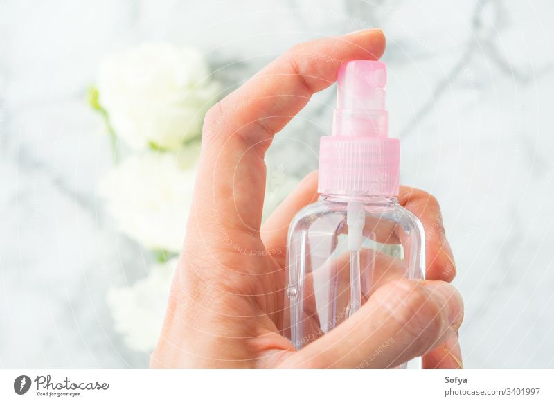 Frauenhand sprüht Flüssigkeit aus Spray über Marmorgrund mit weißen Blumen Flasche liquide Hand spritzend klein rosa Behaarung Produkt Hintergrund Schönheit
