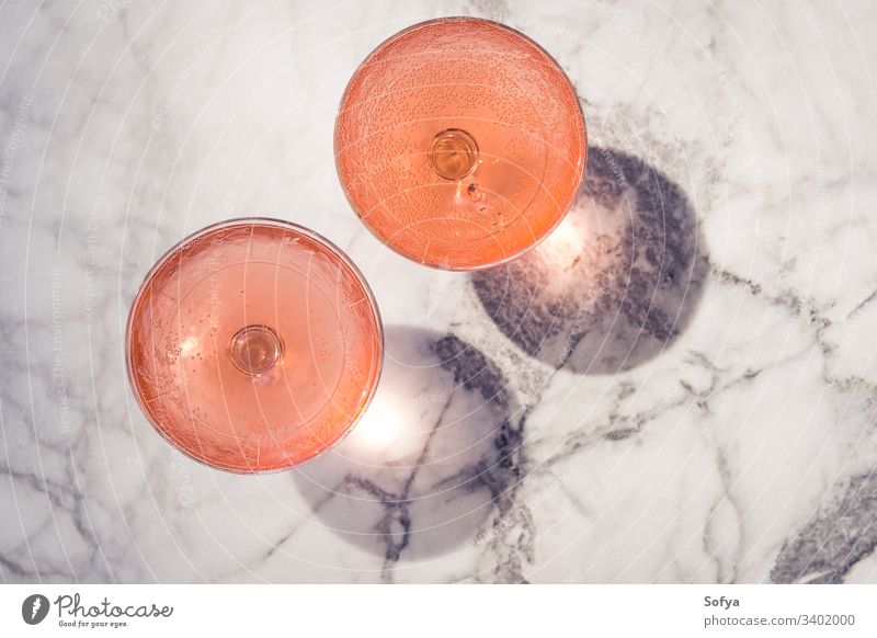 Zwei Kristallstielgläser mit Rosenwein im Freien auf Marmortisch in hartem Licht, das Schatten erzeugt Wein Roséwein weiß Glas Murmel Party rosa trinken