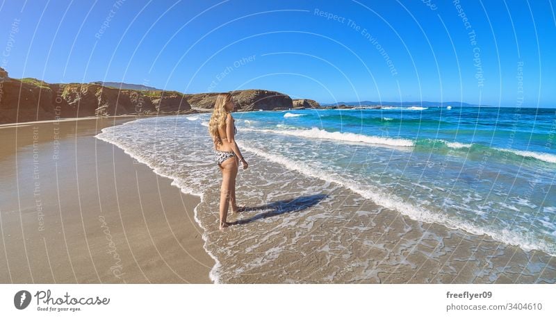 Junge Frau betritt den Ozean an einem Strand mit Klippen in Galicien Tourismus wandern Galicia Spanien Ribadeo Castros Illas Felsen atlantisch Bucht touristisch