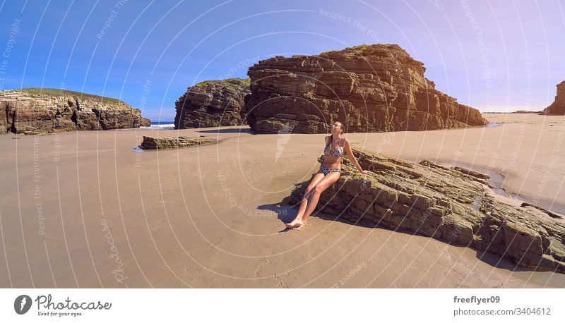Junge Frau im Bikini, die auf einem Felsen an einem Strand voller Klippen sitzt Tourismus wandern Galicia Spanien Ribadeo Castros Illas atlantisch Bucht