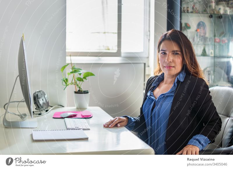 Exekutive Frau in ihrem Büro mit großen Fenstern, durch die das Licht einfällt. Business Geschäftsfrau Computer Laptop jung Menschen Sitzen arbeiten