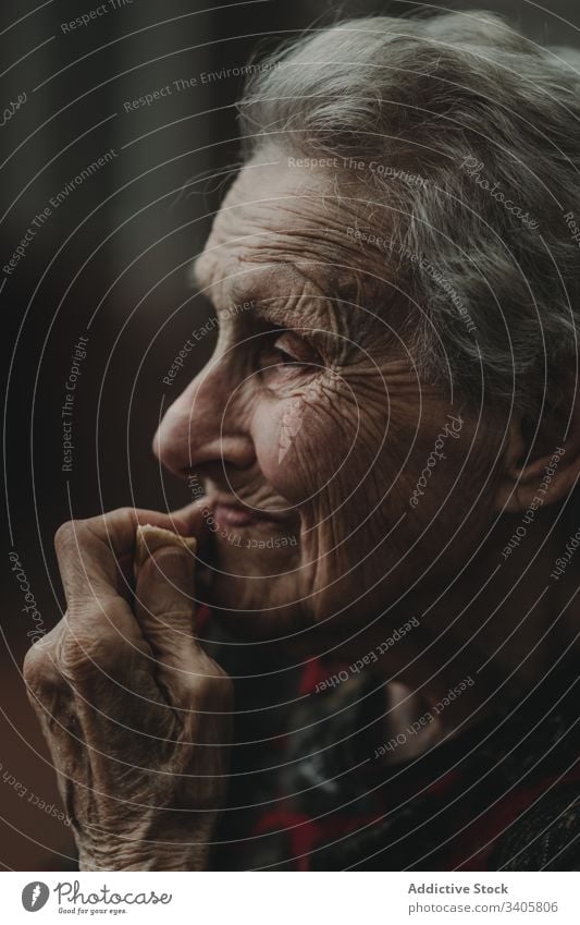 Nachdenkliche ältere Frau berührt Gesicht und isst Kekse Hautfalten Gesicht berühren erinnern Gedächtnis besinnlich ruhig graues Haar Art Vorschein