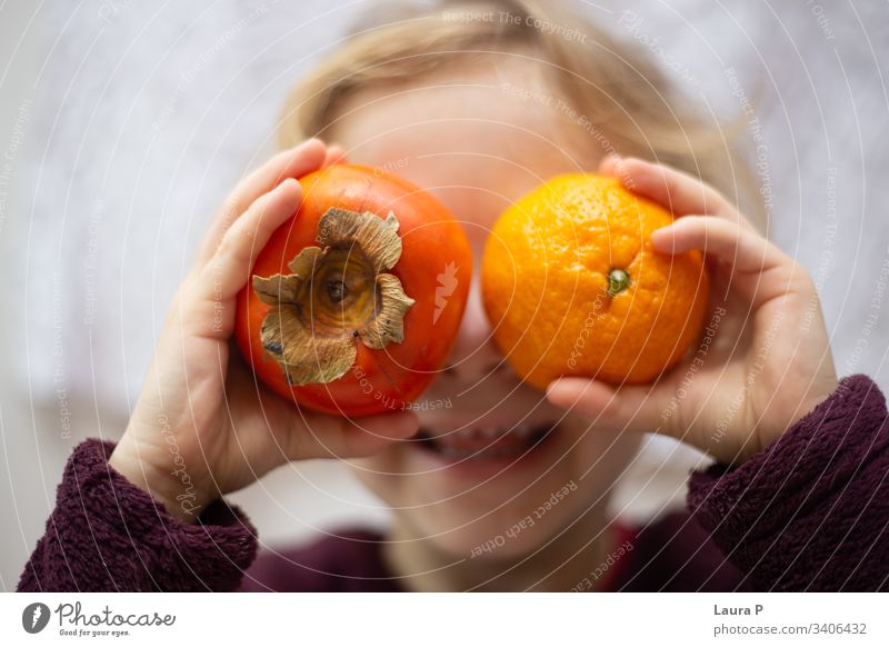 Kleines Mädchen hält eine Kiwi und eine Orange vor ihren Augen und lacht niedlich wenig Kind Spielen Spaß Lachen Lächeln Früchte orange Hände versteckend